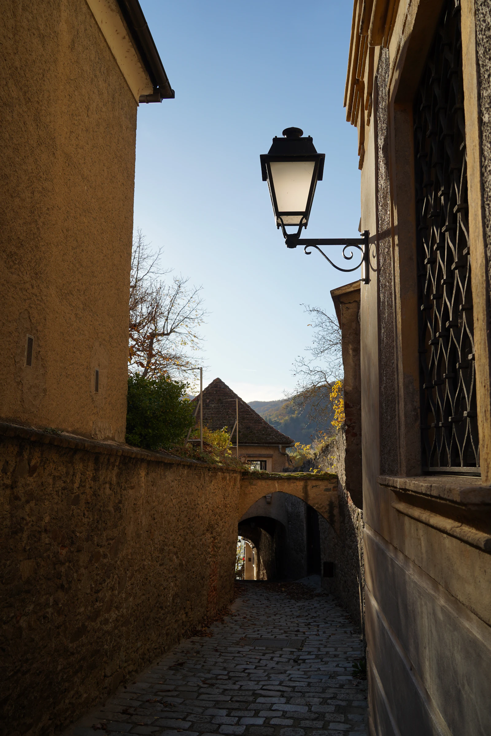 Travel photograph: A narrow stone lane in Dürnstein passing beneath an old wall lamp.