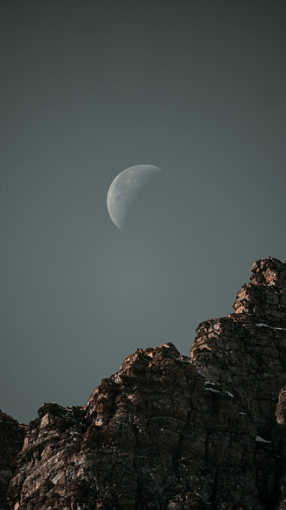 Una mezza luna si vede sopra una montagna rocciosa