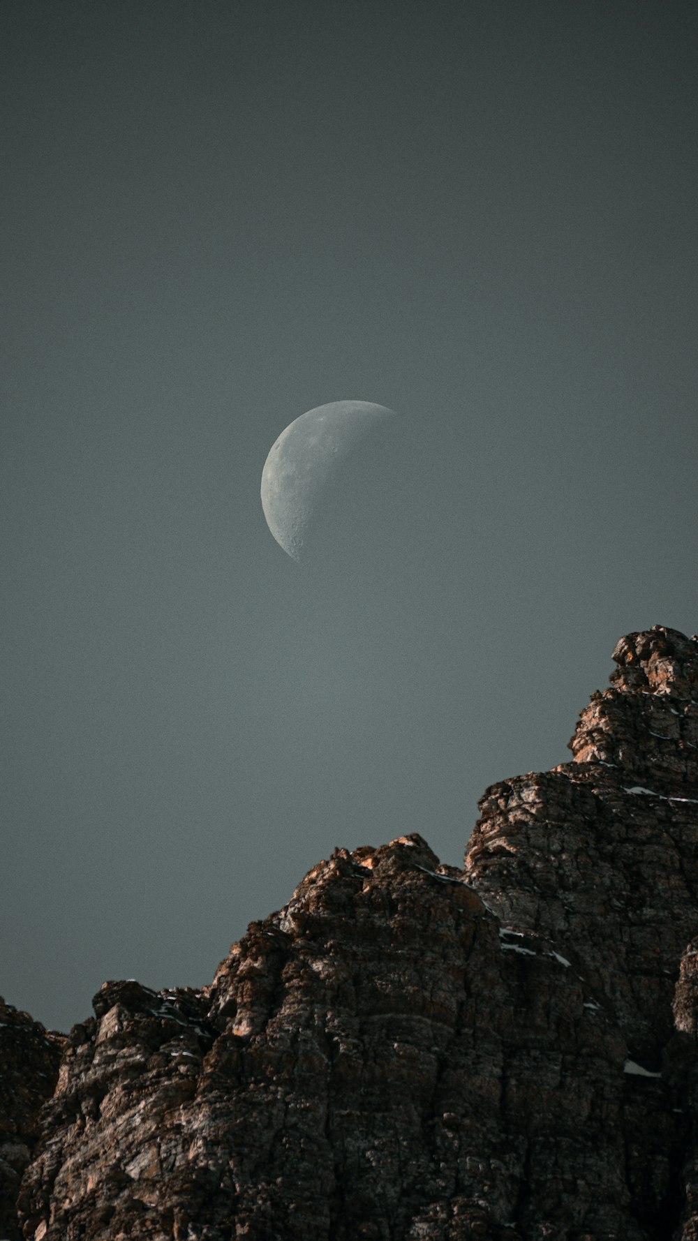 a half moon is seen over a rocky mountain