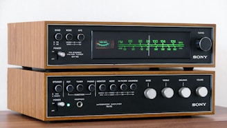 A vintage Sony stereo system consisting of an AM-FM tuner and an integrated amplifier. The devices have a classic design with a wood finish and metallic knobs for controls. The tuner displays a frequency range, and both components feature the brand name prominently.