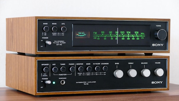 A vintage Sony stereo system consisting of an AM-FM tuner and an integrated amplifier. The devices have a classic design with a wood finish and metallic knobs for controls. The tuner displays a frequency range, and both components feature the brand name prominently.