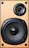 A close-up view of a wooden speaker with a large black woofer and a smaller tweeter. The speaker has a natural wood finish and is secured with screws. 