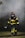 A firefighter, dressed in full gear including a helmet and a protective mask, walks through a smoky environment. The uniform is black with bright yellow reflective strips. The firefighter appears to be carrying a tool, possibly an axe, and the setting suggests an emergency scene with smoke in the air.