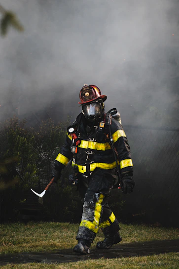 Close-up of a firefighter wearing an SCBA mask fitted with a rugged protective cover in a smoky training environment.