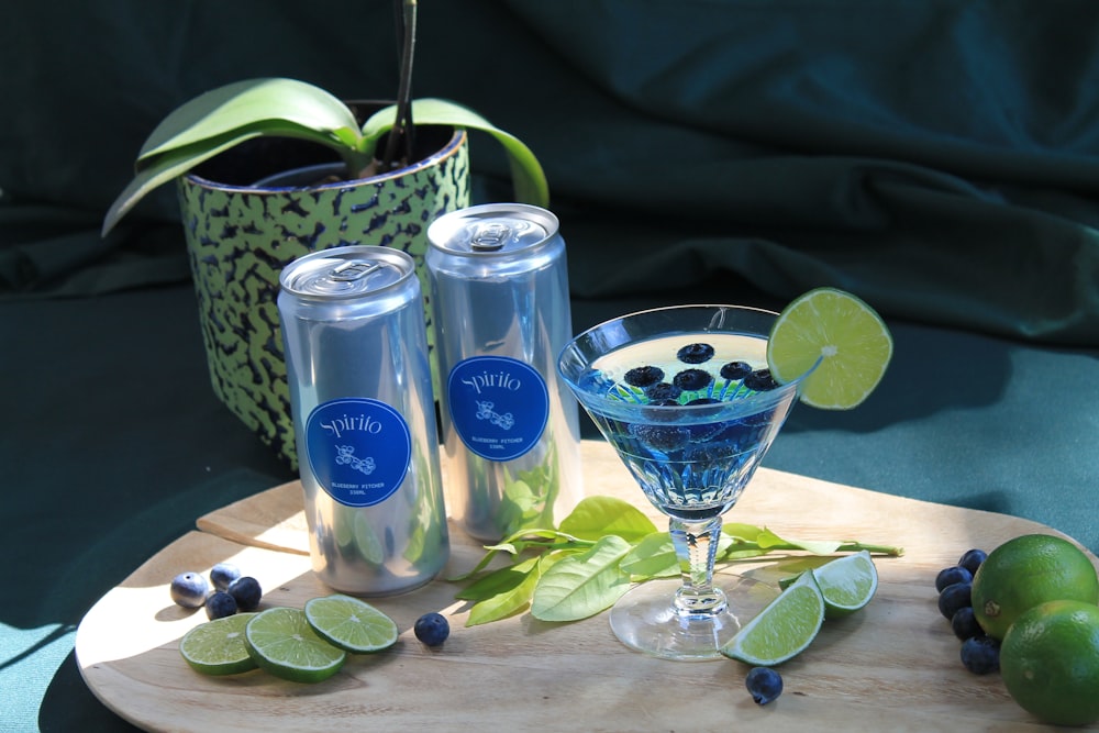 a glass filled with blueberries and limes next to a can of soda