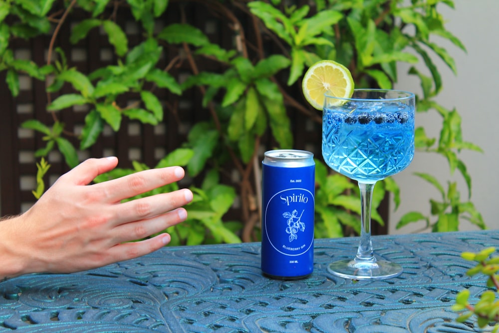 a hand reaching out towards a blue drink on a table