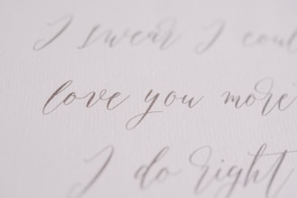 Elegant handwritten script in a soft, flowing style, featuring phrases like 'love you more' on a textured, white background.