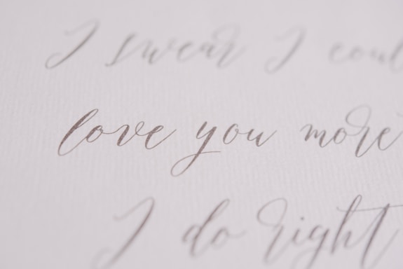 Elegant handwritten script in a soft, flowing style, featuring phrases like 'love you more' on a textured, white background.