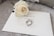 A white rose lies delicately on an elegant wedding invitation card labeled 'Bride & Groom.' Two silver rings rest beside the rose, adding a touch of elegance and romance to the setup.