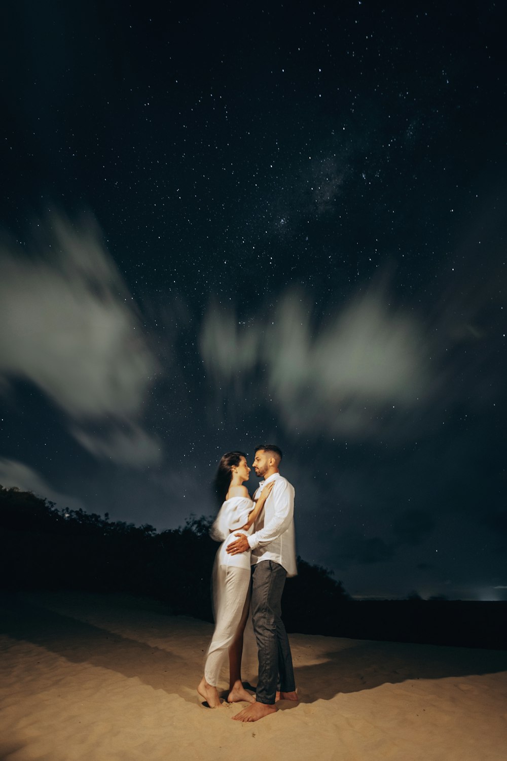 a man and woman standing in the sand under a night sky