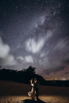 Romantic couple under a starry night sky with zodiac signs above.