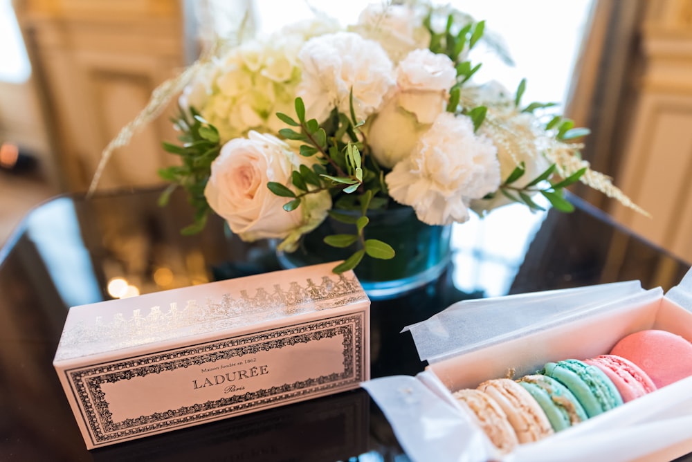 a box of macaroons sitting on a table next to a vase of flowers