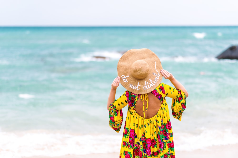 a woman with a hat on her head standing on the beach