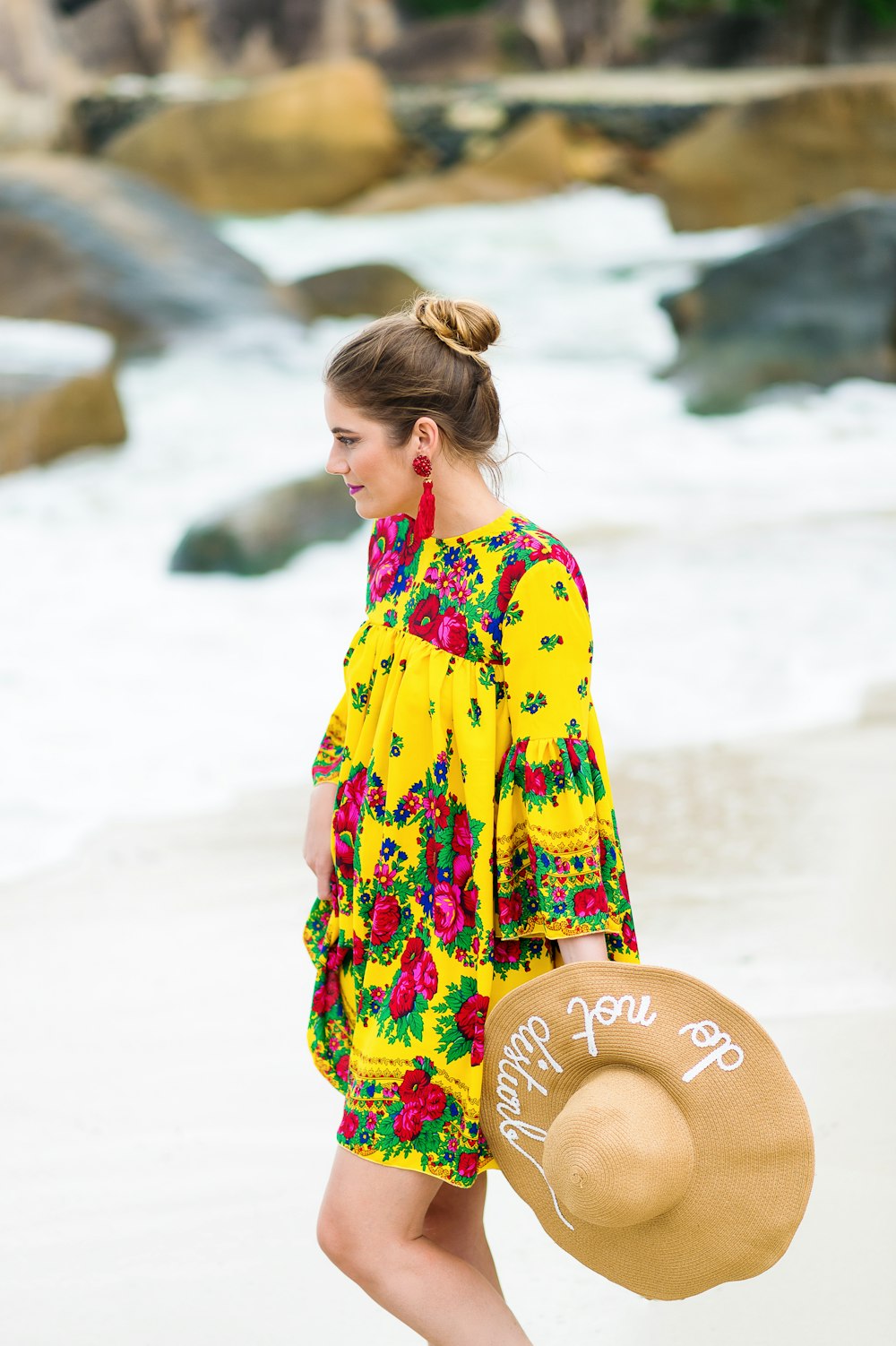 a woman walking on the beach with a hat