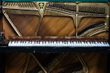 An open piano showcasing its internal strings and felt hammers above the keyboard. The metal frame and tuning pegs are visible, highlighting the craftsmanship and intricate design of the instrument's interior.