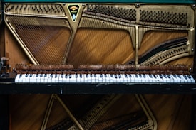 An open piano showcasing its internal strings and felt hammers above the keyboard. The metal frame and tuning pegs are visible, highlighting the craftsmanship and intricate design of the instrument's interior.