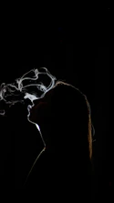Silhouette of a woman exhaling smoke against black