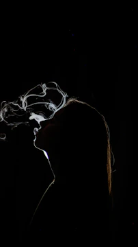 Silhouette of a woman exhaling smoke against black