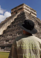 a man wearing a hat standing in front of a pyramid