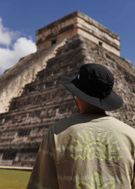a man wearing a hat standing in front of a pyramid