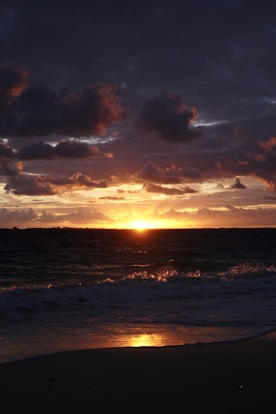the sun is setting over the ocean on a cloudy day