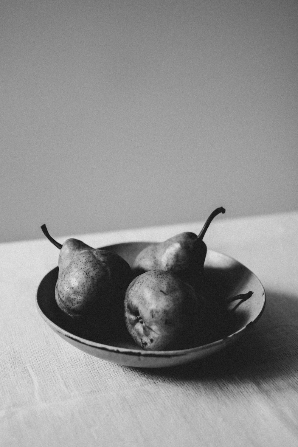 three pears in a bowl on a table