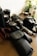 A collection of photography equipment on a wooden surface, including two DSLR cameras, camera lenses, a camera strap, lens cases, and a few miscellaneous items. A small potted plant and a bottle of lotion or cleaning solution are also visible in the background.