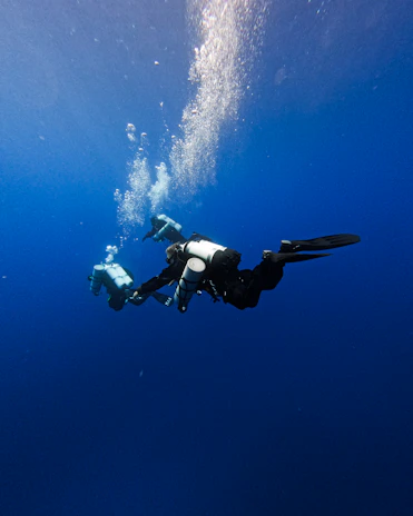 Three scuba divers are swimming underwater in the deep blue ocean. They are equipped with scuba gear and are surrounded by bubbles rising to the surface.