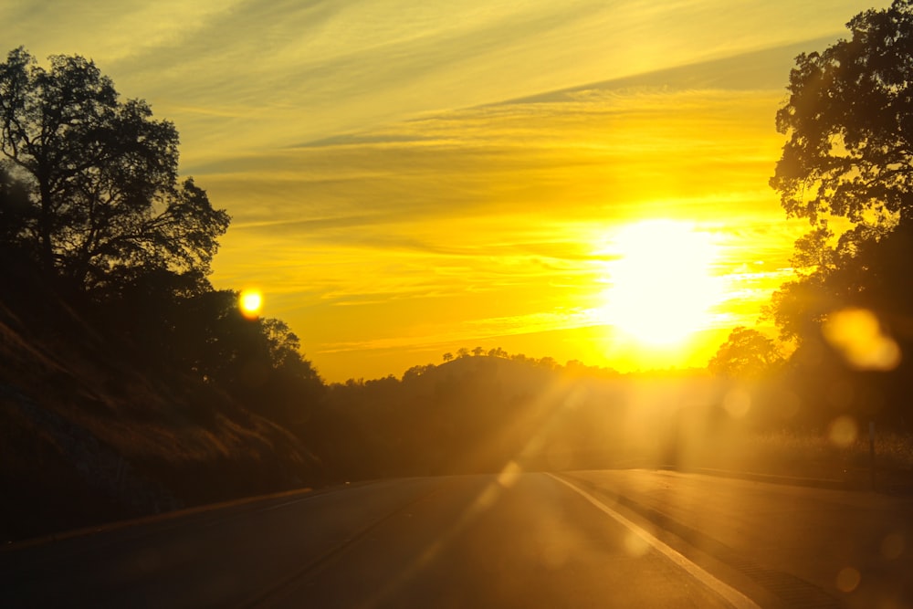 the sun is setting over the trees on the side of the road