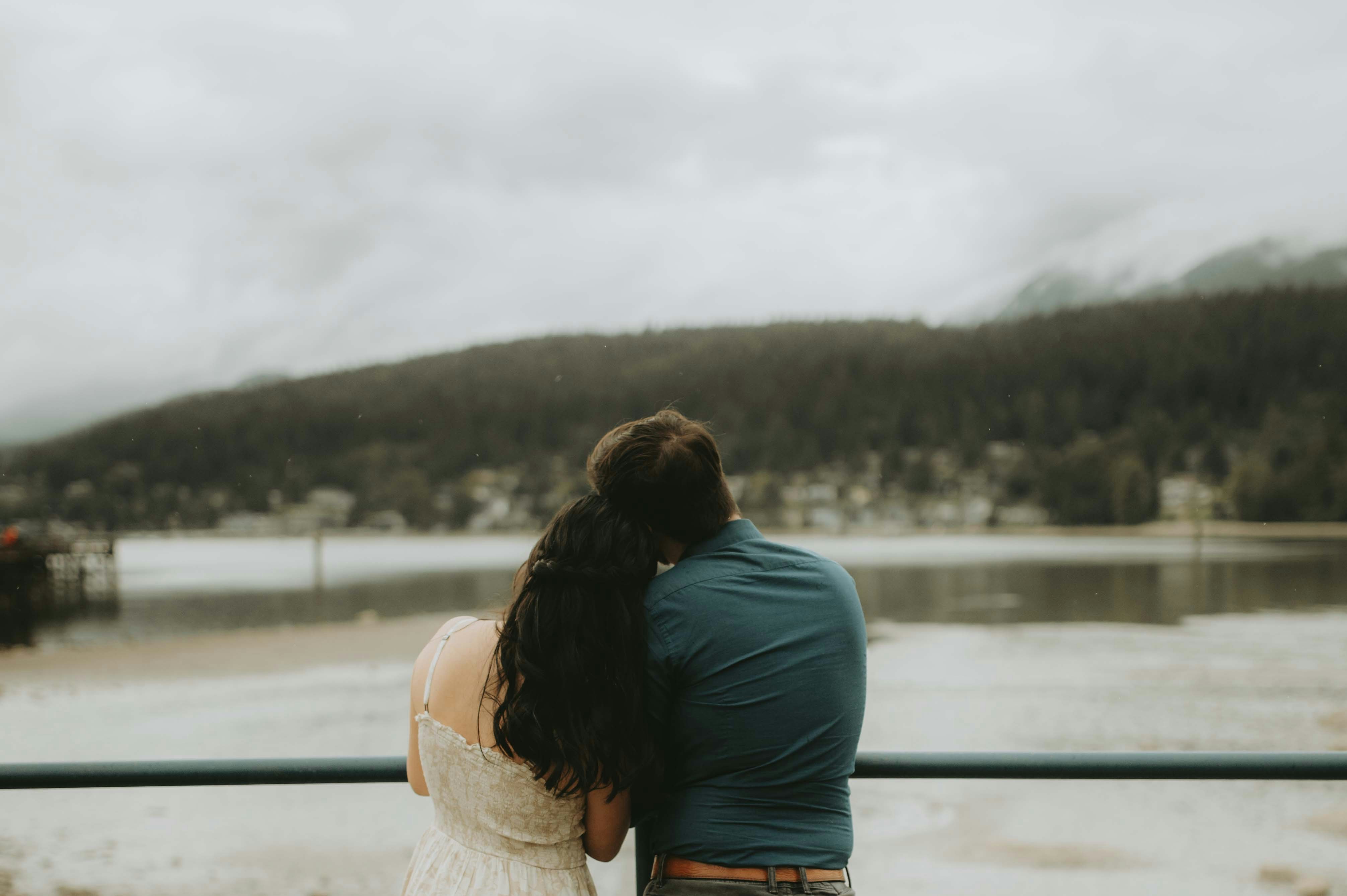 a man and a woman sitting on a bench looking at a lake
