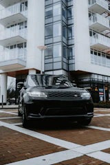 A sleek black Range Rover parked outside an airport terminal at dusk with city lights glowing.