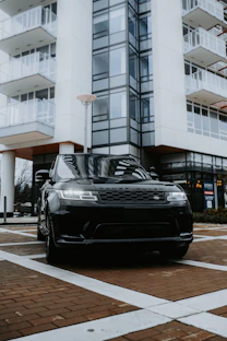 A sleek black Range Rover parked outside an airport terminal at dusk with city lights glowing.