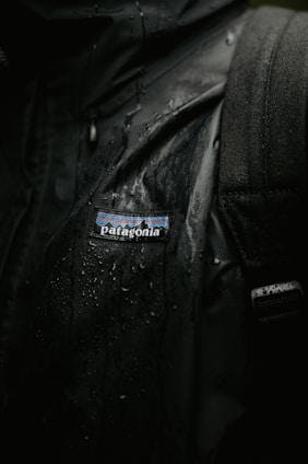 A sleek waterproof jacket hanging on a rustic wooden hook with raindrops on the fabric