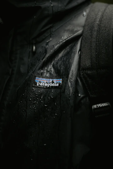 Close-up of a sleek Aquashield waterproof jacket hanging on a wooden hook with raindrops on the fabric.