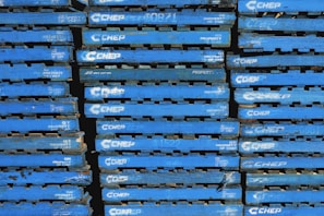 A stack of blue wooden pallets marked with the brand name 'CHEP' in white letters. Each pallet is uniformly colored and arranged tightly together, forming a repetitive pattern.
