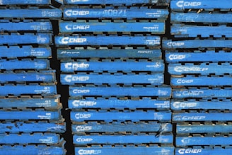 A stack of blue wooden pallets marked with the brand name 'CHEP' in white letters. Each pallet is uniformly colored and arranged tightly together, forming a repetitive pattern.
