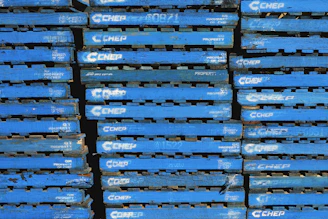 A stack of blue wooden pallets marked with the brand name 'CHEP' in white letters. Each pallet is uniformly colored and arranged tightly together, forming a repetitive pattern.