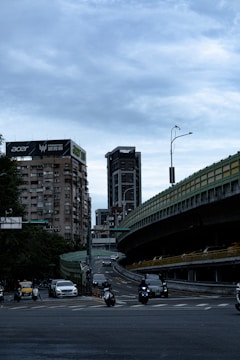 A cityscape featuring high-rise buildings with prominent advertisements, including one for Acer. The scene includes a busy elevated highway with multiple vehicles such as cars and motorcycles. The sky is overcast, contributing to a somewhat dim ambiance.