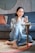A young woman sitting comfortably on a couch, smiling while using her smartphone to chat with friends.
