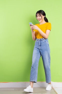 a woman standing against a green wall holding a cell phone