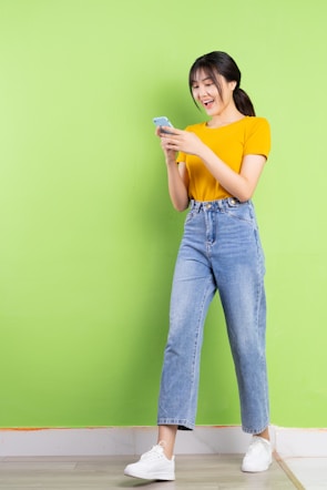 a woman standing against a green wall holding a cell phone