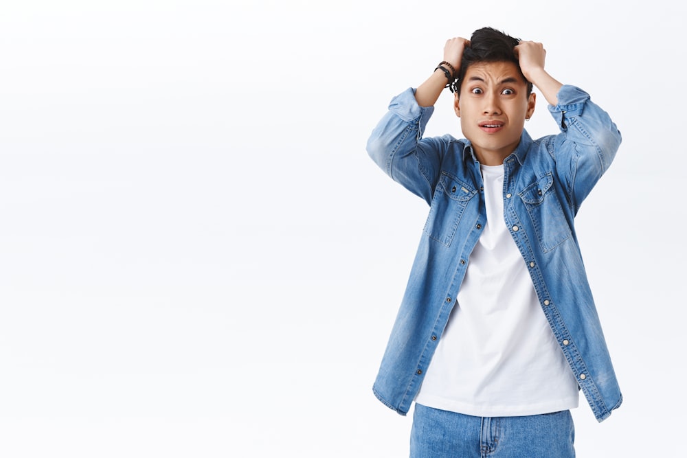 a man in a denim jacket is holding his head with his hands