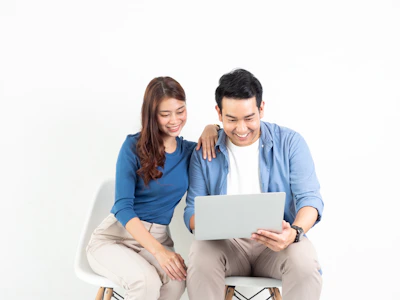 a man and woman sitting on a chair looking at a laptop