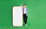 A person stands confidently against a bright green background, leaning on a large, blank smartphone cutout with a red-orange border. They are casually dressed in a blue shirt, white t-shirt, black pants, and white sneakers, and display a positive demeanor.