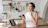 Happy woman in her kitchen next to a washing machine with a thumbs-up gesture