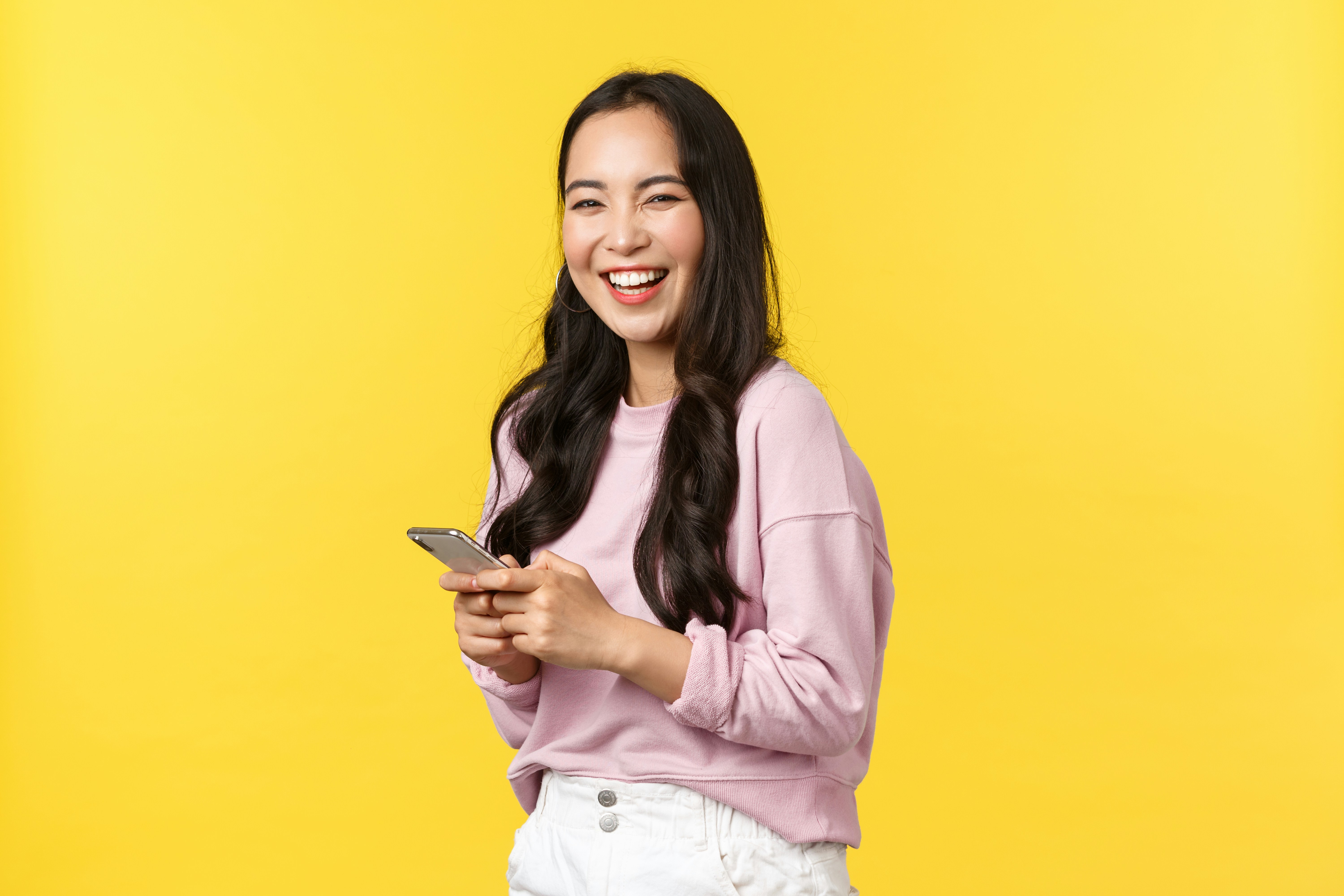 a woman in a pink sweater smiles while looking at her cell phone
