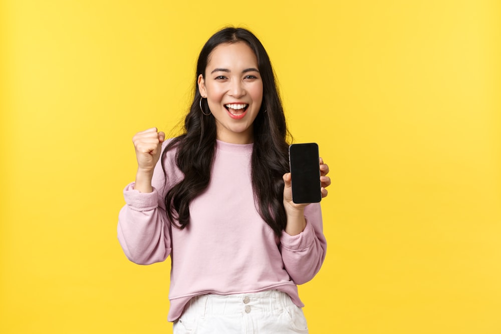 a woman in a pink shirt is holding a cell phone