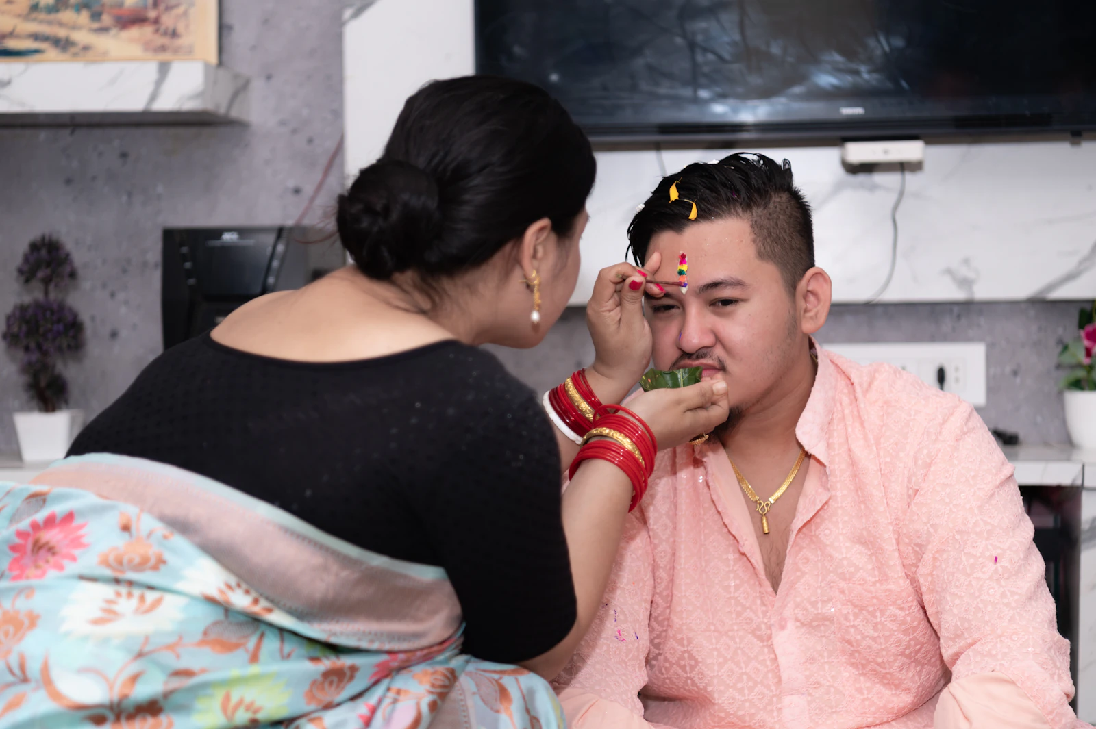 A sister in red bangles pressing tika onto her brother's forehead during Bhai Tika in a Nepali home