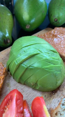 A cheerful green avocado slicer resting on a cutting board with sliced avocados ready to serve.