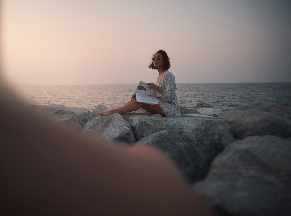 a woman sitting on rocks reading a book
